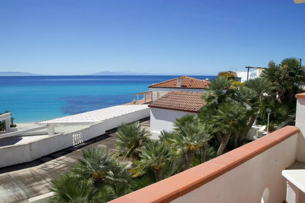 Vista sul mare blu dalla terrazza tra palme e tetti in tegole