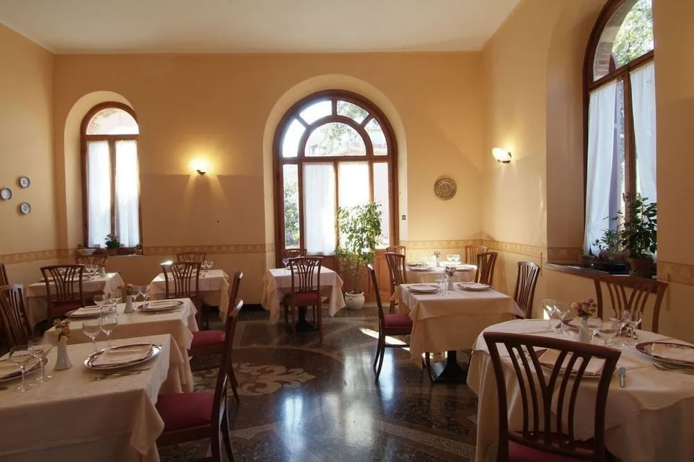 Sala da pranzo luminosa con finestre ad arco, tavoli eleganti e pavimento intarsiato