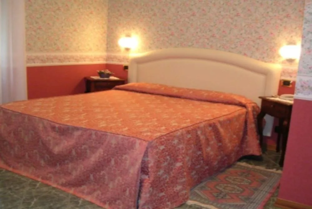 Camera matrimoniale con copriletto rosa, testiera bianca e carta da parati floreale