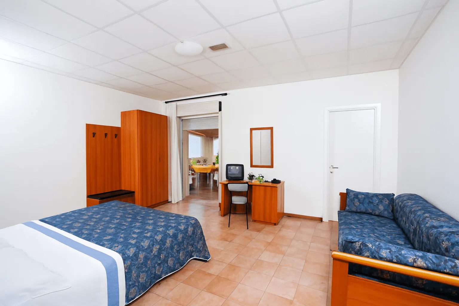 Camera con letto matrimoniale, divano blu, scrivania e armadio in legno