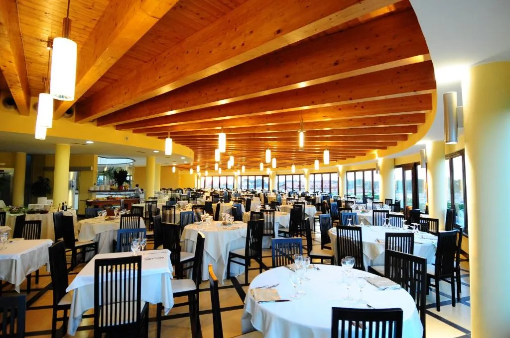 Sala ristorante con soffitto in legno, tavoli apparecchiati e ampie vetrate