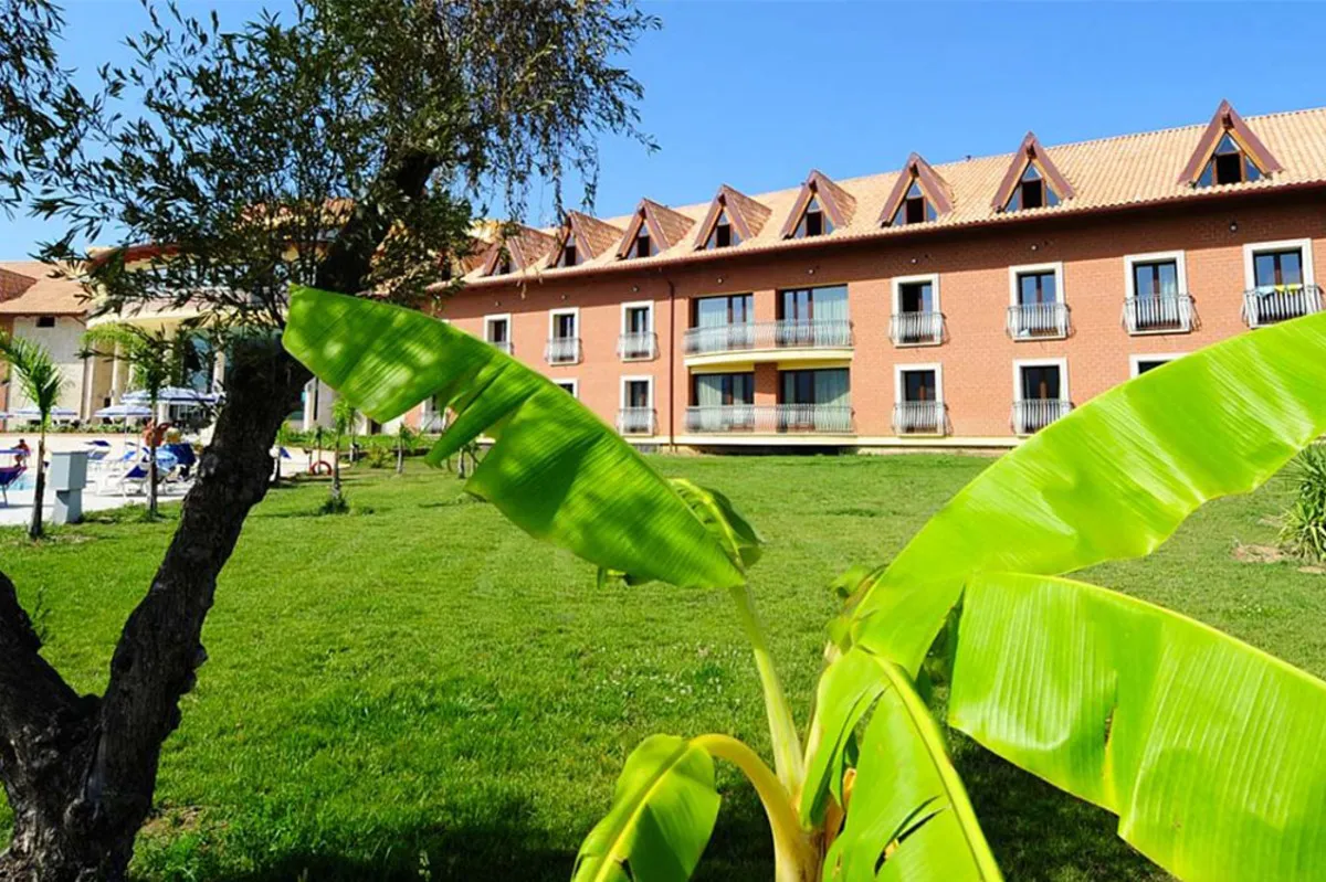 Edificio dell'hotel in mattoni con prato verde e piante tropicali in primo piano