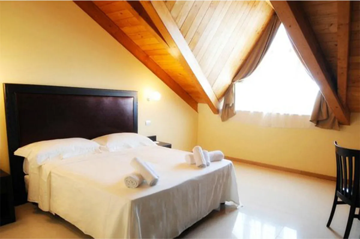 Camera mansardata con soffitto in legno, letto matrimoniale bianco e finestra