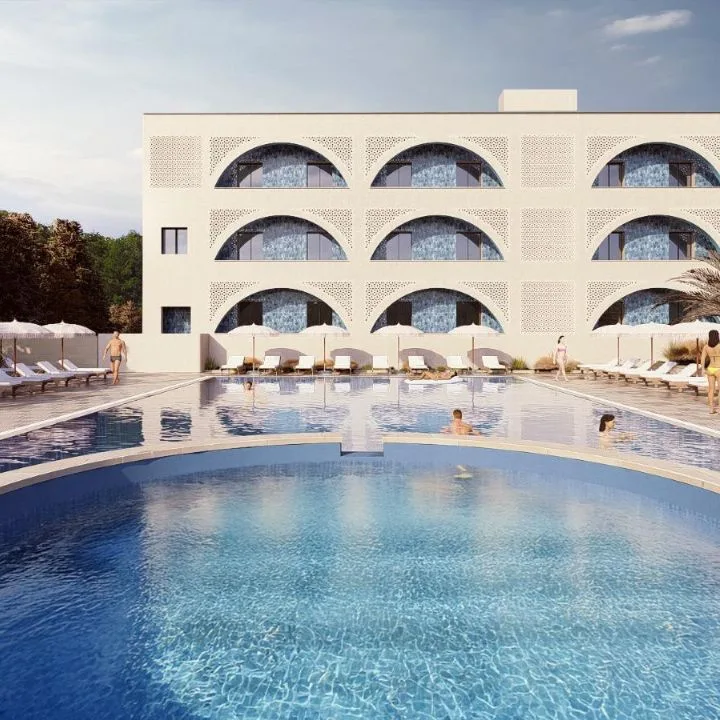 Piscina dell'hotel con acqua azzurra, facciata ad archi sullo sfondo e ospiti tra lettini e ombrelloni