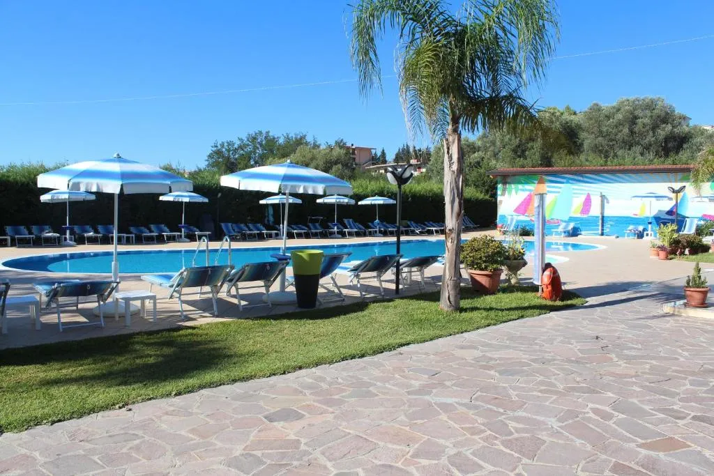 Piscina con lettini, ombrelloni a strisce e palma sul prato