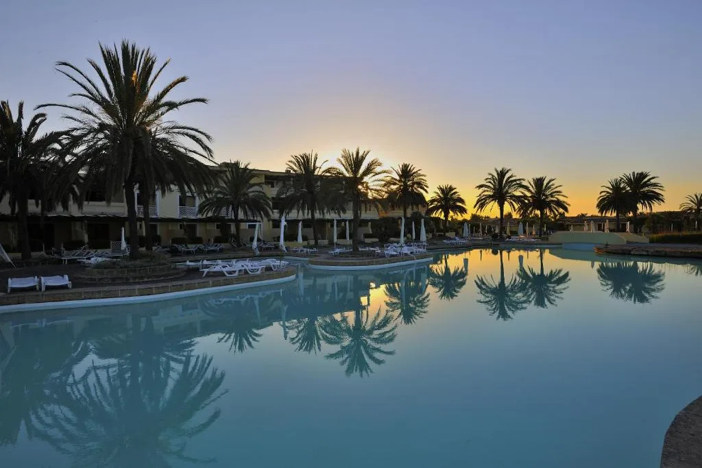 Piscina del resort al tramonto con palme riflesse nell'acqua e cielo colorato
