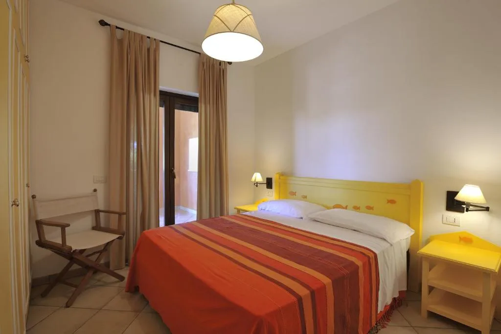 Camera da letto con testiera gialla, copriletto a righe arancioni e accesso al balcone
