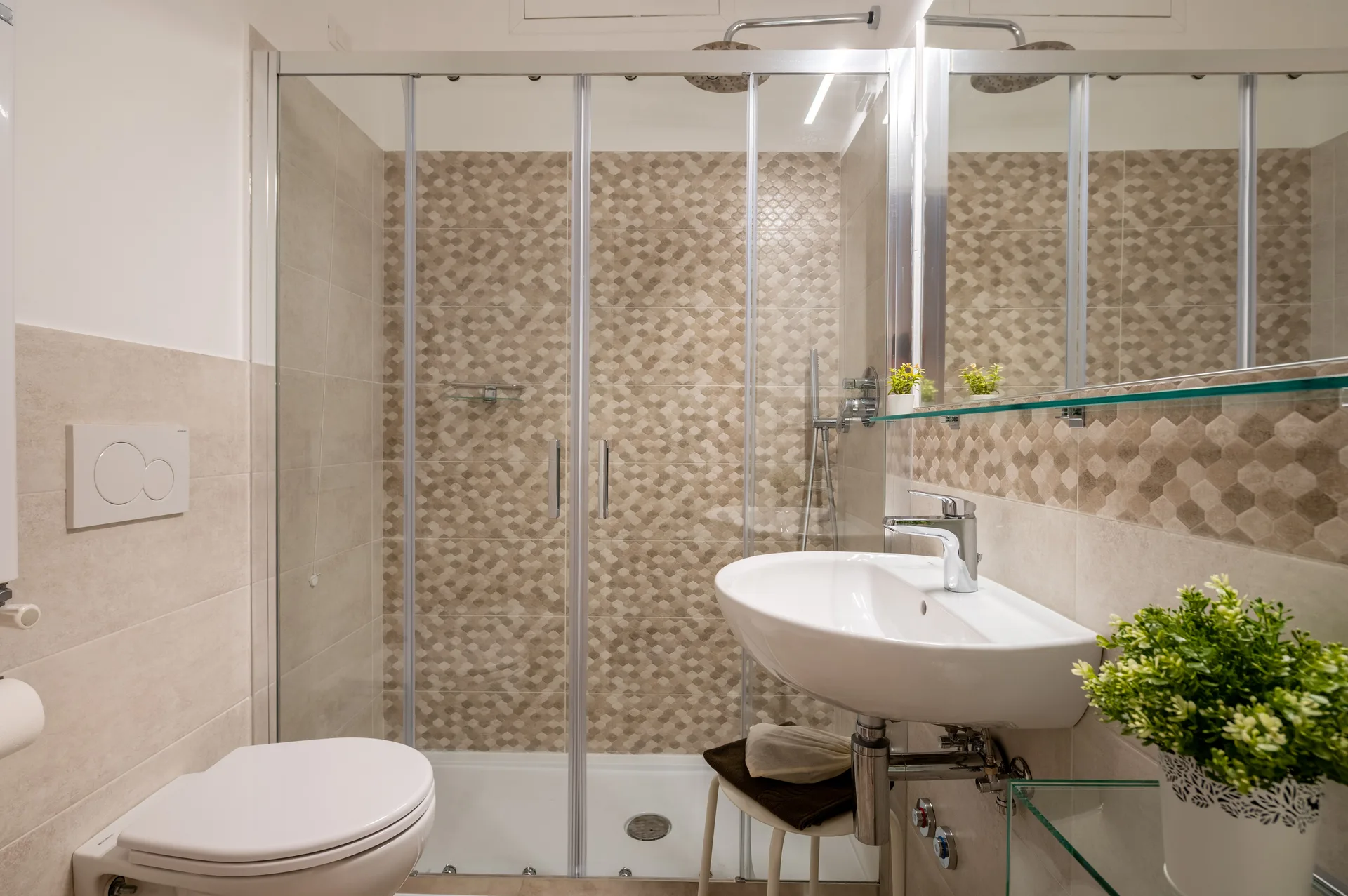 Bagno moderno con doccia in vetro, lavabo bianco e piastrelle decorative beige