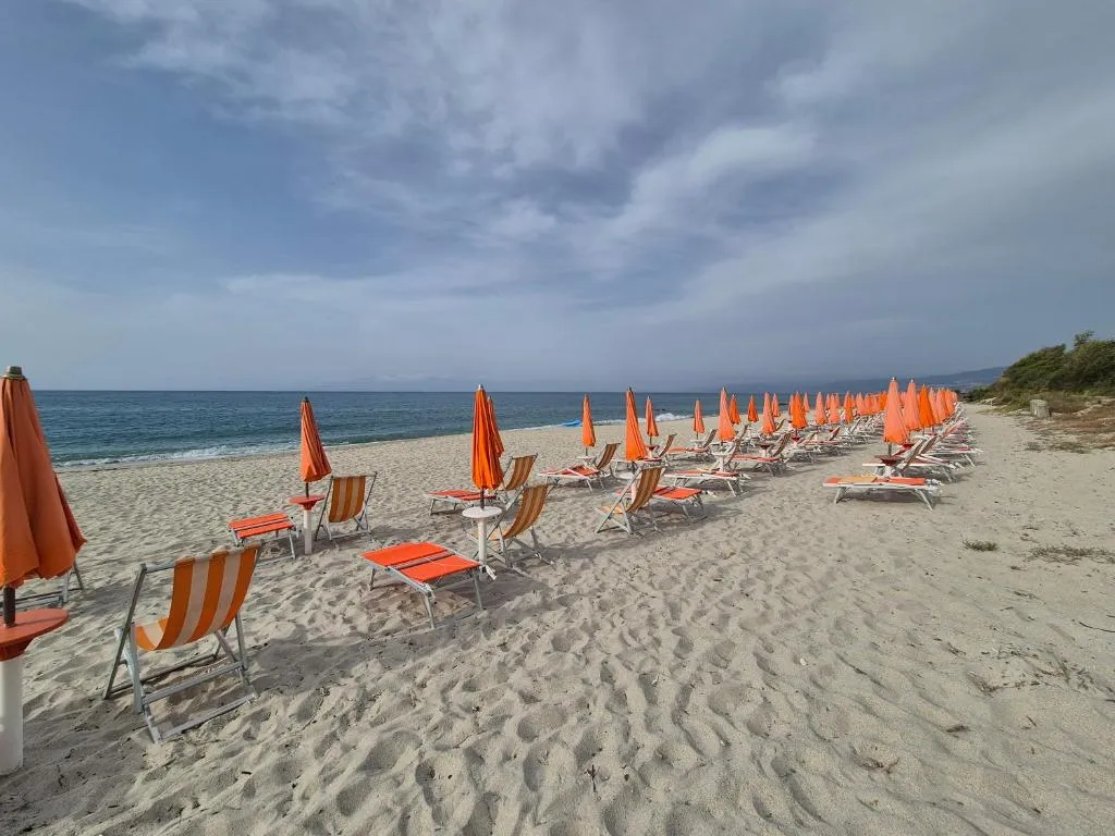 Spiaggia con lettini e ombrelloni arancioni chiusi sotto cielo nuvoloso