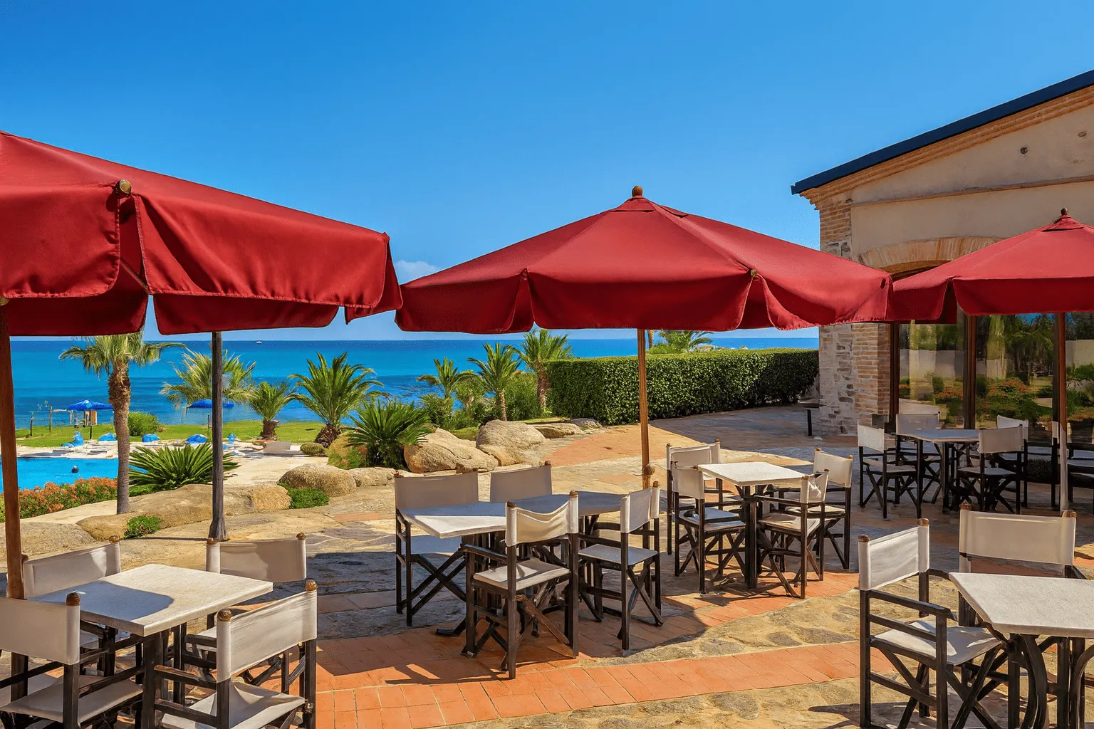 Terrazza ristorante con ombrelloni rossi, tavoli e vista sul mare e sulla piscina