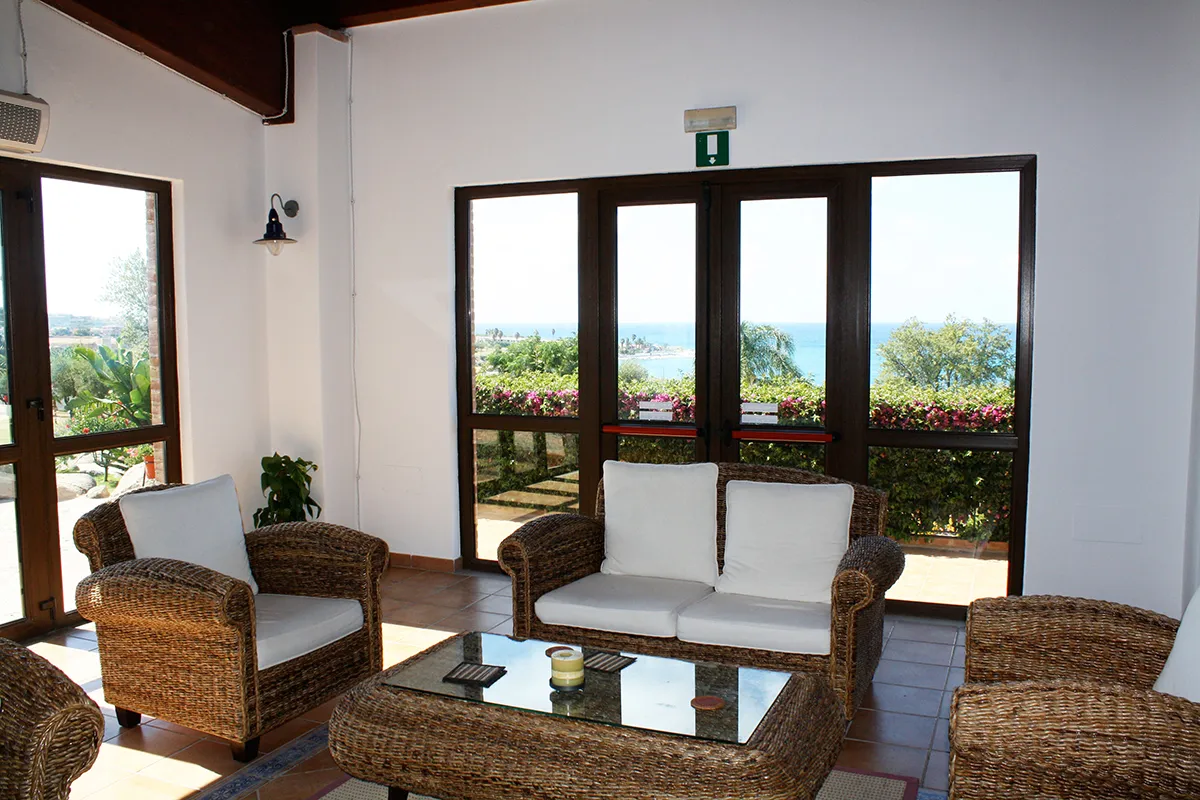 Salotto interno con poltrone in vimini, divano bianco e grandi vetrate vista mare
