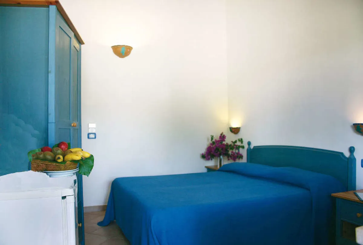 Camera matrimoniale con copriletto blu, armadio e cestino di frutta