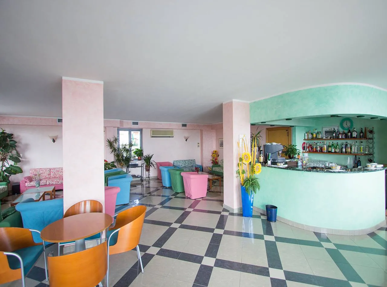 Hall dell'hotel con bar verde, poltrone colorate e pavimento a scacchi