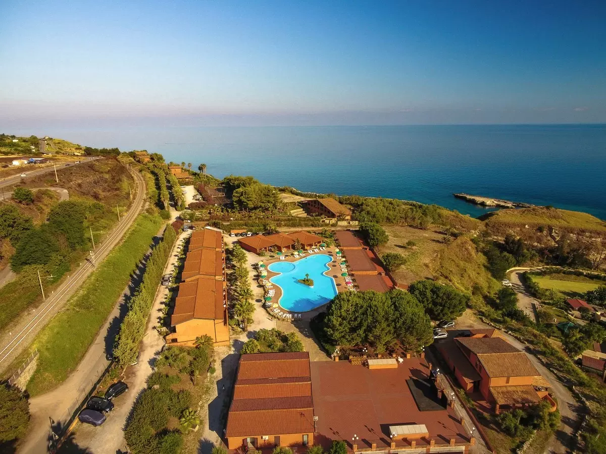 Vista aerea del resort sulla scogliera con piscina e mare blu all'orizzonte