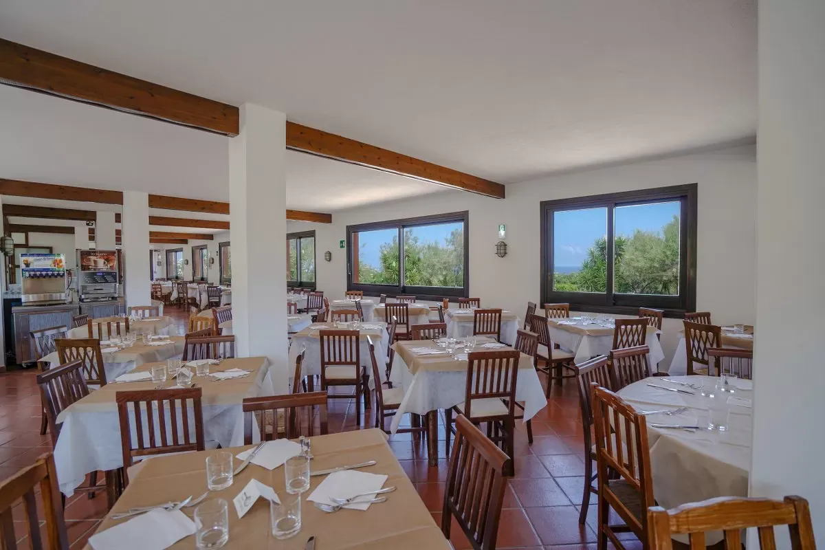 Sala ristorante con tavoli apparecchiati e ampie finestre con vista sul verde
