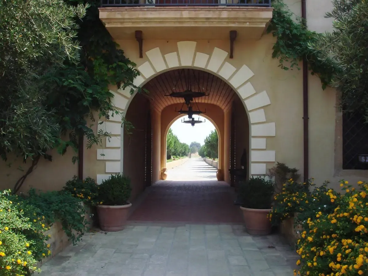 Arco d'ingresso in pietra con lanterne e vasi di fiori gialli che conduce al giardino