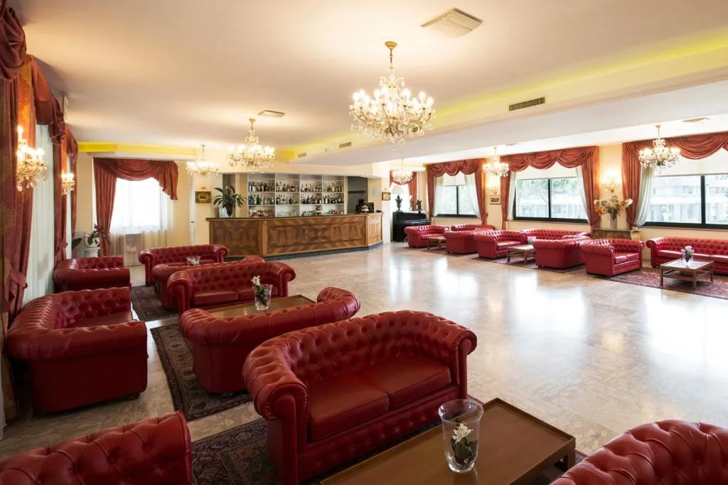 Salone con poltrone in pelle rossa, bar in legno e lampadari di cristallo