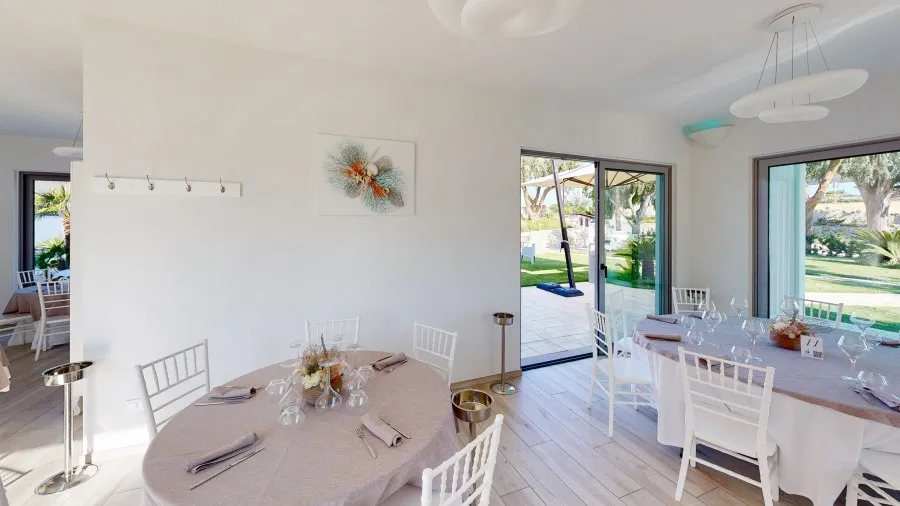 Sala ristorante luminosa con tavoli rotondi apparecchiati e vetrate affacciate sul giardino