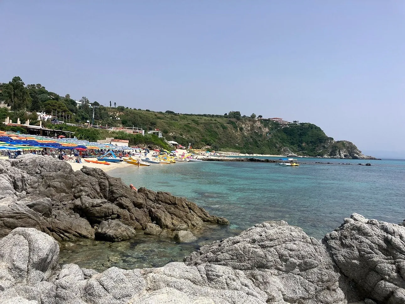 Cala con scogli, spiaggia attrezzata con ombrelloni colorati e mare turchese