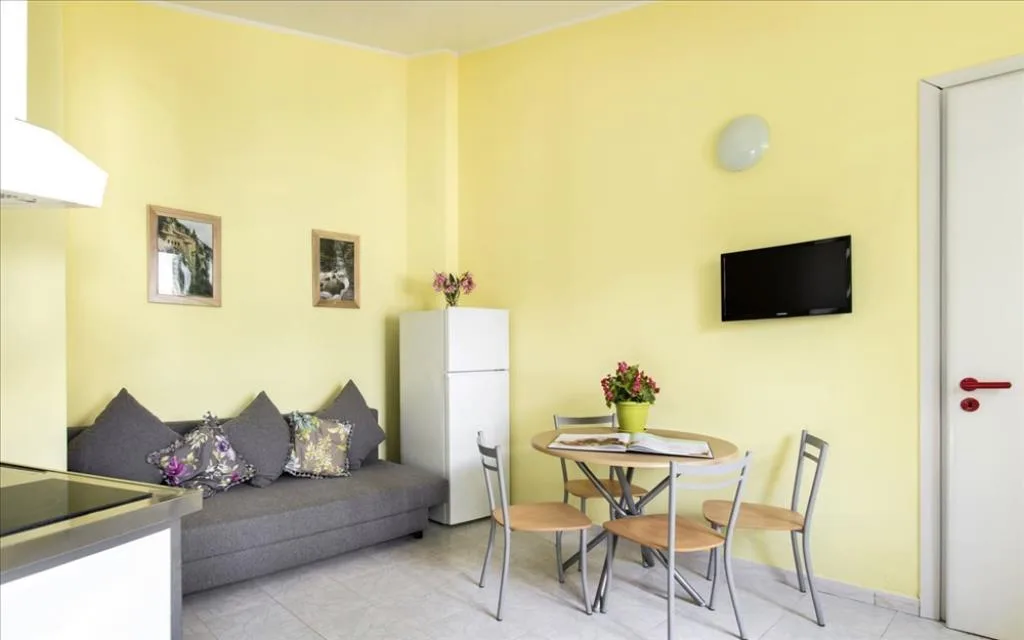 Soggiorno con divano grigio, tavolo da pranzo, frigorifero e TV a parete su parete gialla