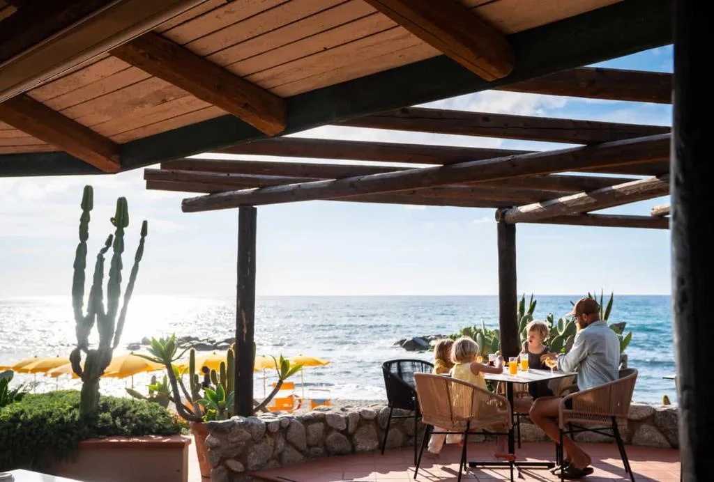 Famiglia a tavola sotto pergolato in legno con vista panoramica sul mare e la spiaggia