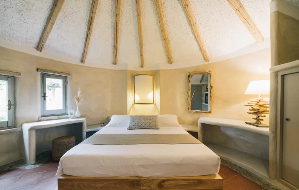 Camera in stile rustico con soffitto a travi in legno, pareti color sabbia e letto matrimoniale