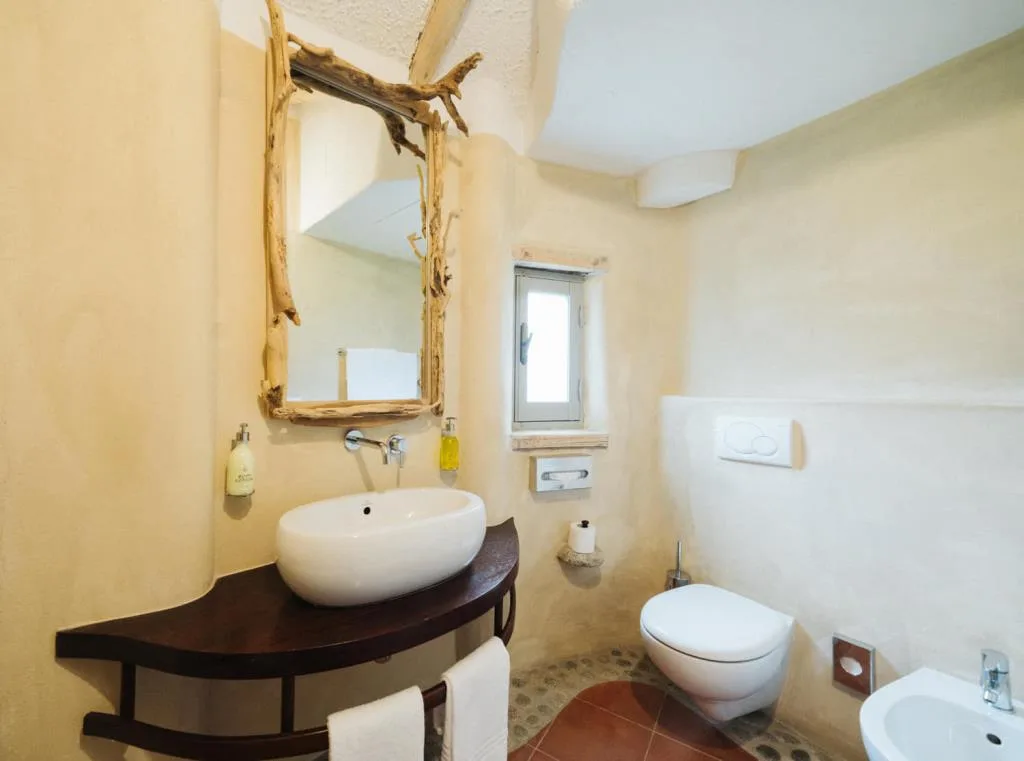 Bagno in stile rustico con lavabo bianco, specchio in legno di mare e parete color sabbia