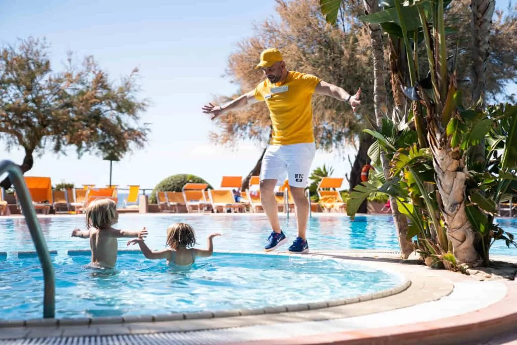 Animatore in maglietta gialla gioca con bambini nella piscina per bimbi del resort