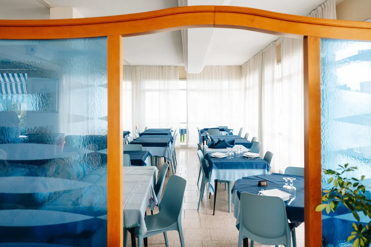 Sala ristorante con tavoli apparecchiati con tovaglie blu e sedie azzurre