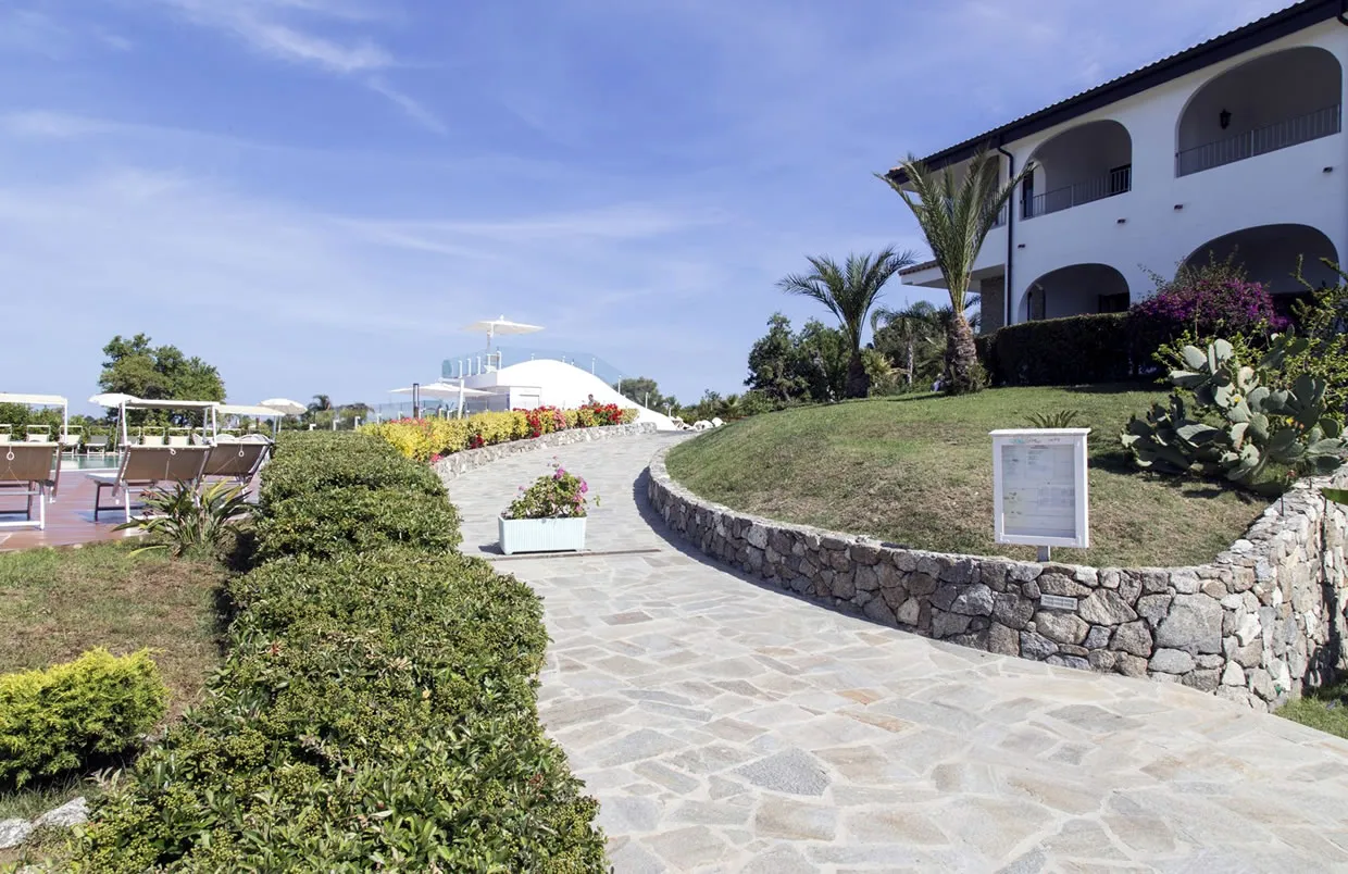 Vialetto in pietra del resort tra giardini curati ed edificio bianco con archi