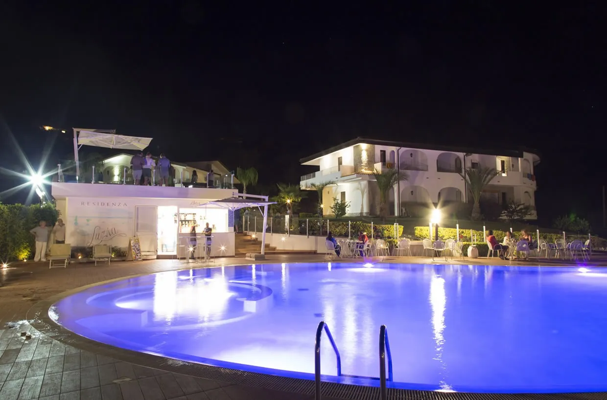 Piscina illuminata di notte con bar Residenza Luzia e ospiti nei tavoli