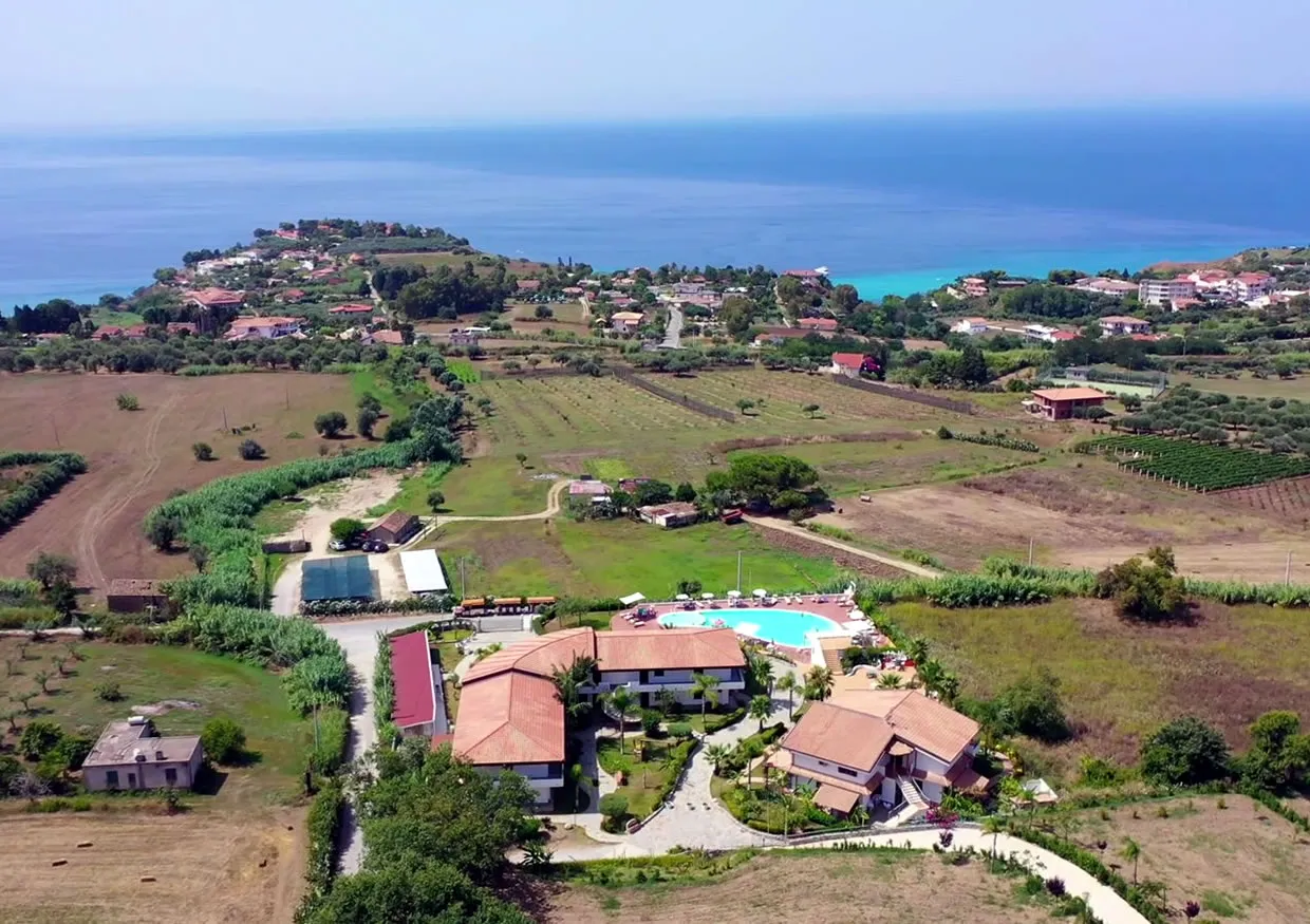 Vista aerea del resort immerso nella campagna con piscina e mare turchese sullo sfondo