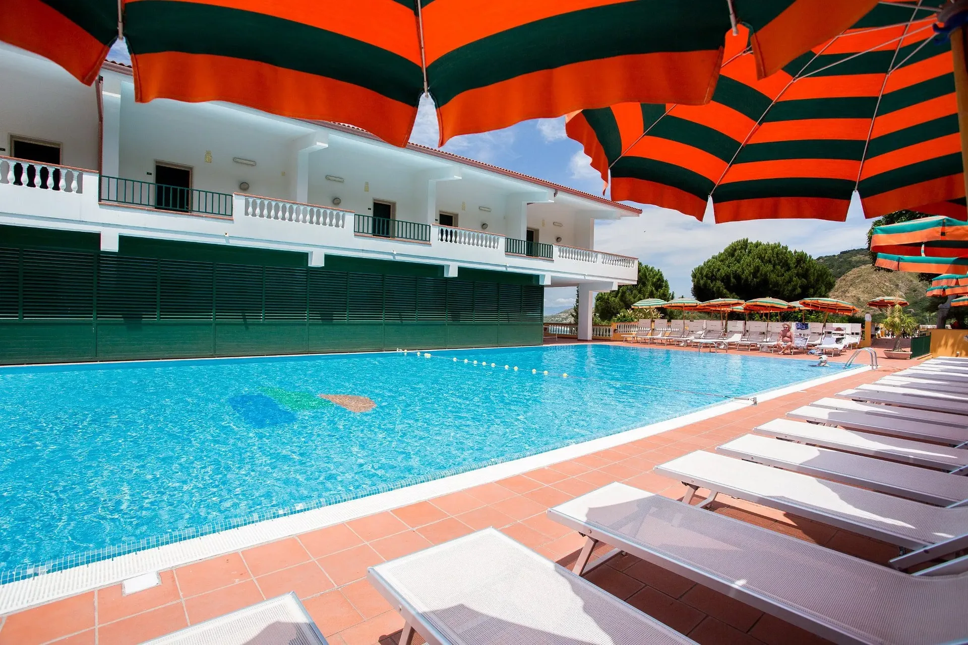 Piscina dell'hotel vista da sotto gli ombrelloni a righe arancioni e verdi