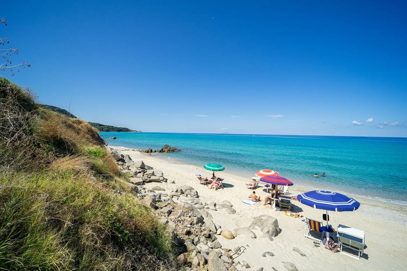 Spiaggia di sabbia con ombrelloni colorati e mare turchese cristallino
