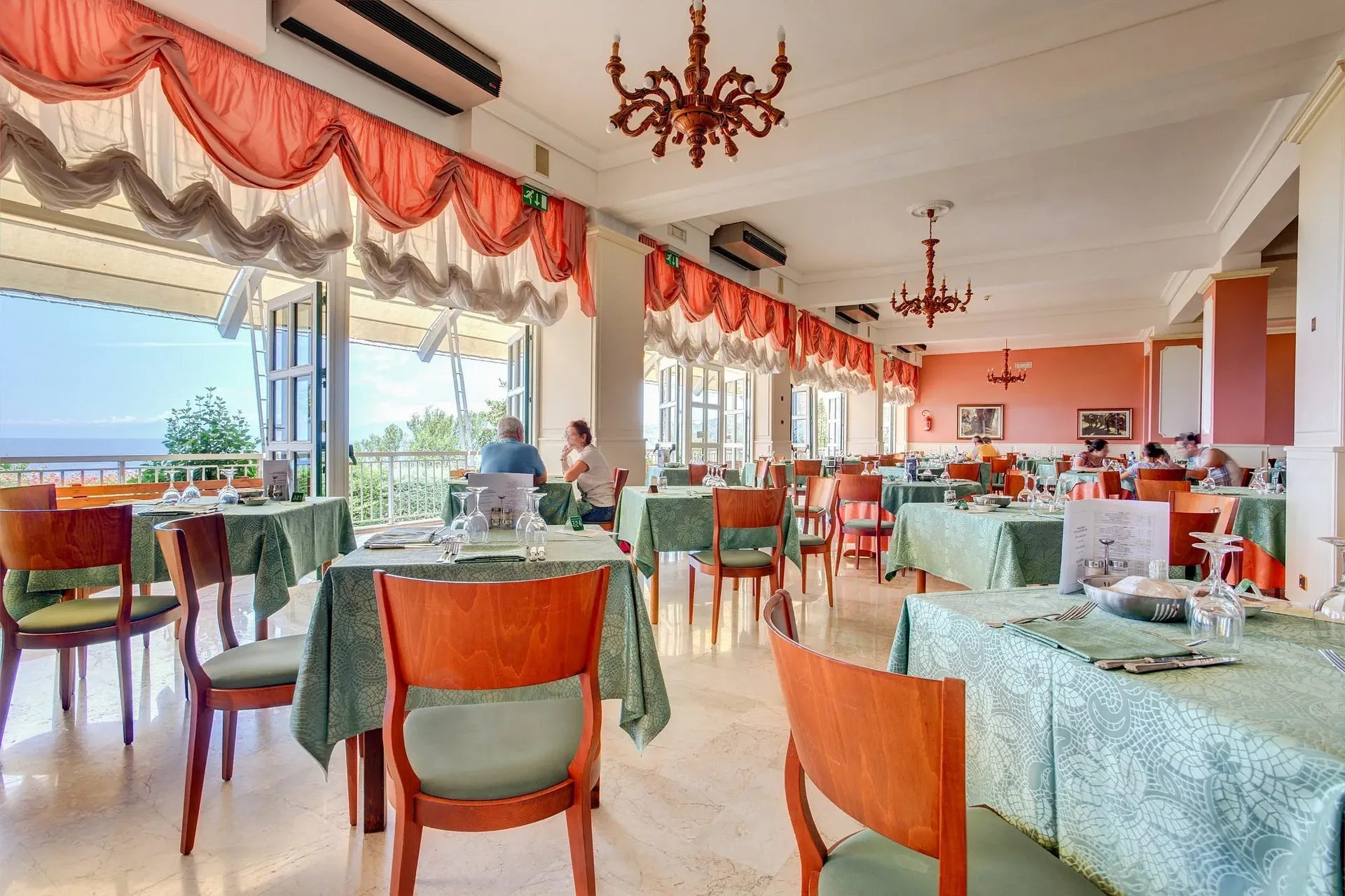 Sala ristorante con tavoli apparecchiati e grandi finestre sul mare