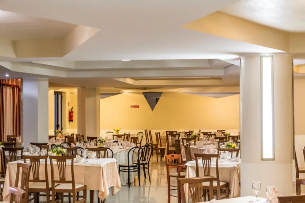 Ampia sala da pranzo con colonne, tavoli rotondi apparecchiati e pavimento lucido
