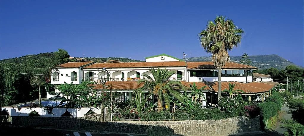Vista esterna dell'hotel circondato dal verde con palme e colline sullo sfondo