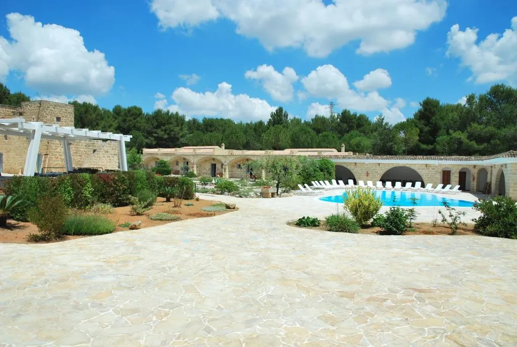 Vasta corte pavimentata in pietra con giardino e piscina della masseria