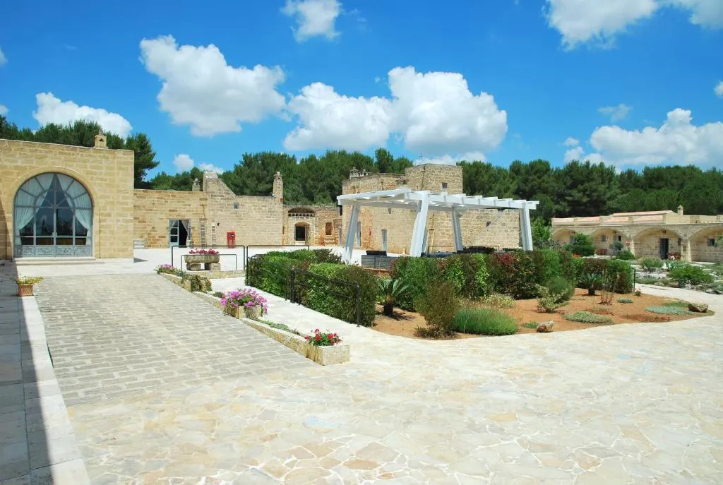 Cortile della masseria con pergolato bianco, giardino fiorito e edifici in pietra