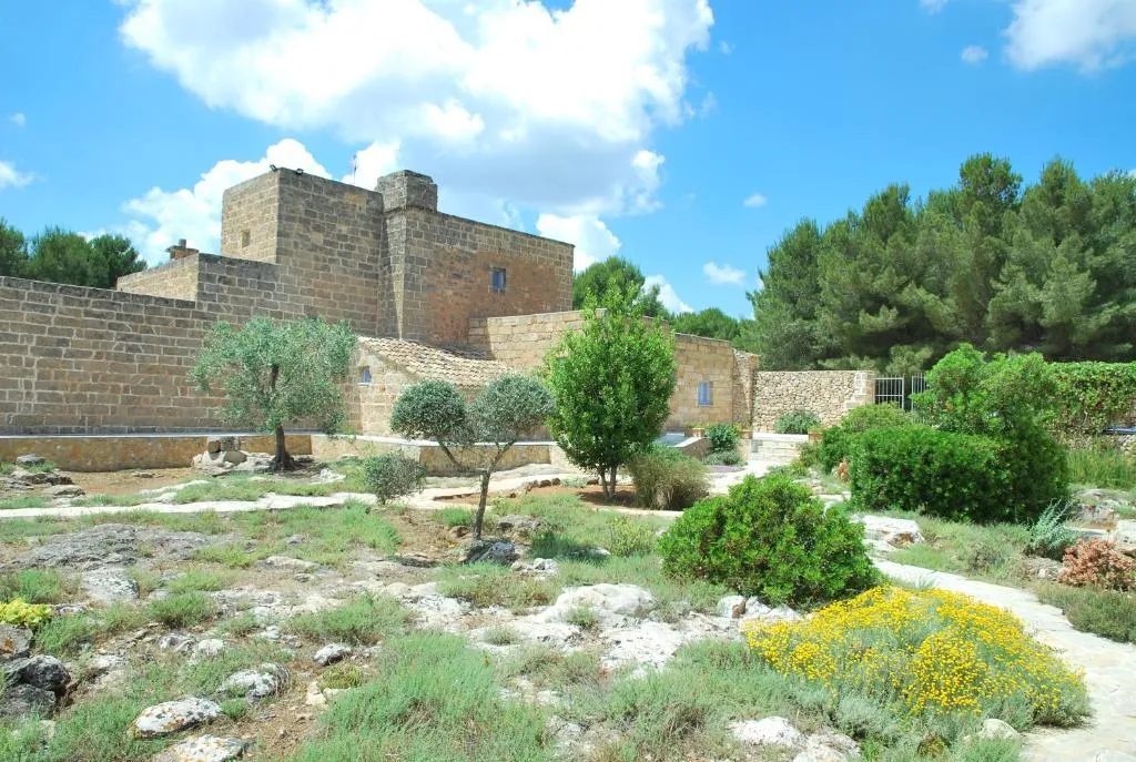 Esterno della masseria in pietra immerso nel verde con giardino roccioso mediterraneo