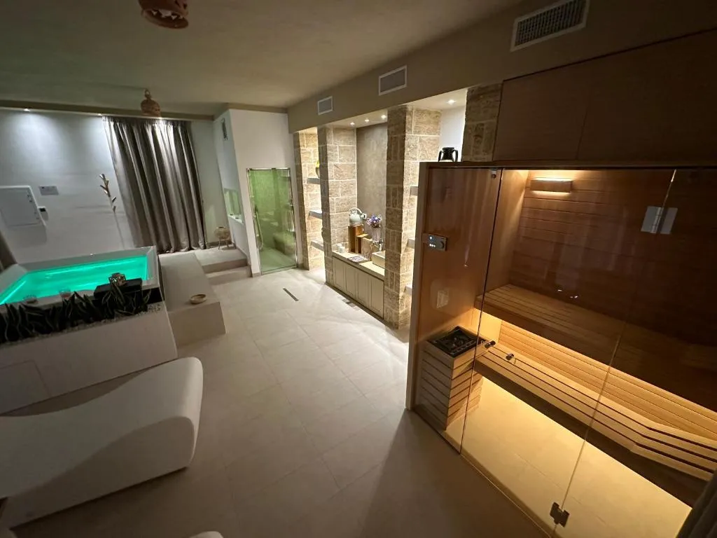 Spa con sauna in legno illuminata, vasca idromassaggio e pareti in pietra