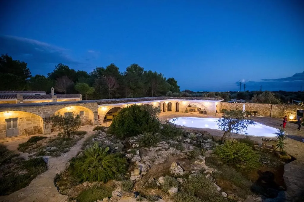 Masseria illuminata di sera con piscina e giardino al crepuscolo