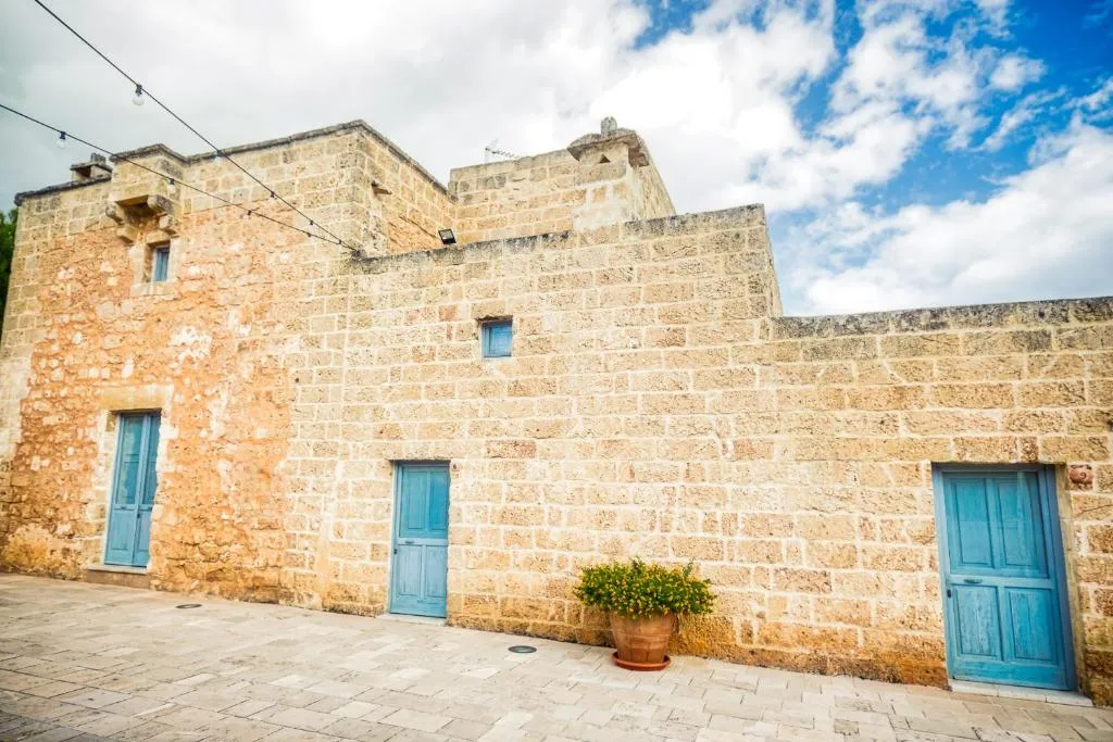 Facciata in pietra della masseria con porte azzurre e cielo nuvoloso