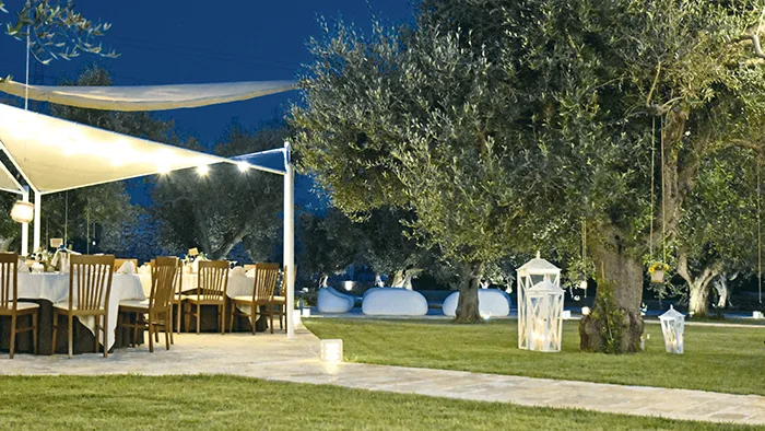 Area ristorante all'aperto illuminata di sera tra ulivi e lanterne