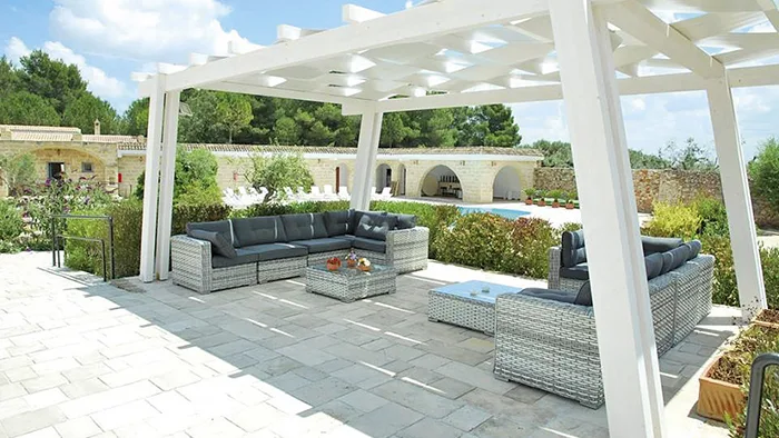 Pergolato bianco con divani in rattan e vista sulla piscina della masseria