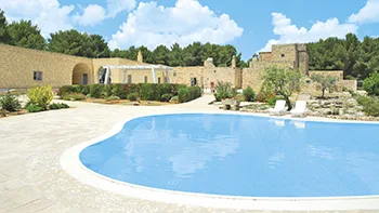 Piscina curva con vista sugli edifici in pietra e giardino mediterraneo
