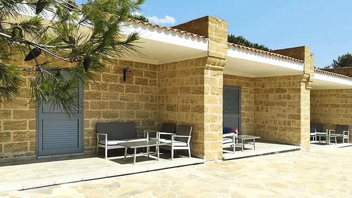 Portico esterno in pietra con divanetti e poltrone sotto un pino
