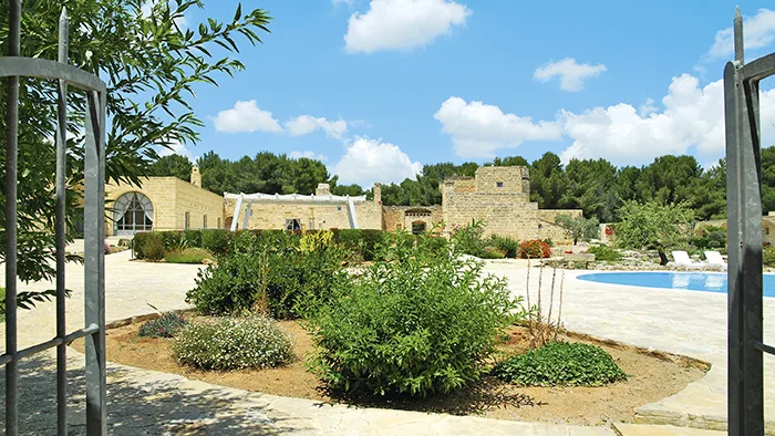 Giardino curato con vegetazione mediterranea e masseria in pietra sullo sfondo