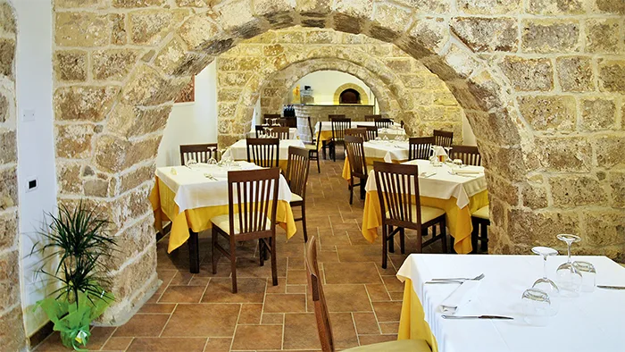Sala ristorante interna con volte in pietra e tavoli apparecchiati con tovaglie gialle