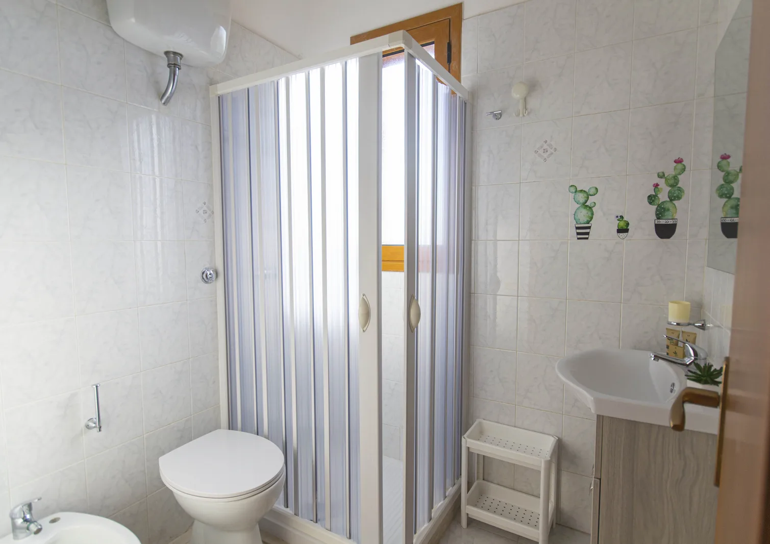 Bagno con box doccia, sanitari, lavabo e piastrelle chiare decorate con cactus